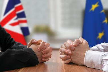 Two men facing each other at a table with EU and UK flags in the background