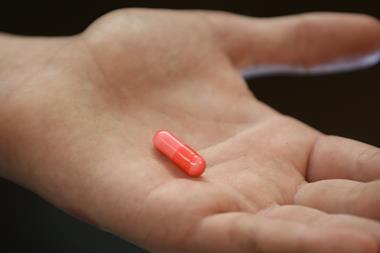 An image showing a hand holding a pink pill