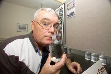 A photograph of George Aldrich sniffing a bottle of colourless liquid