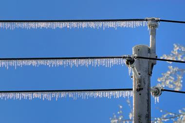 Icicles on row of powerlines after ice storm, against blue sky