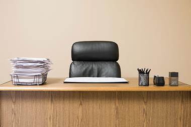 An office desk with a full in tray and an empty chair