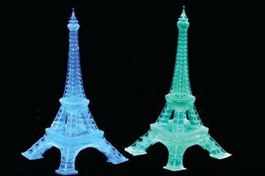 Two models of the Eiffel Tower int he dark one is luminescent blue and the other is luminescent green