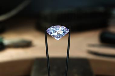 A photo showing a polished and cut diamond, sparkling as it is being held between a pair of tweezers
