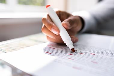 An image showing the hand of a person holding a red marker pen and proof reading a paper