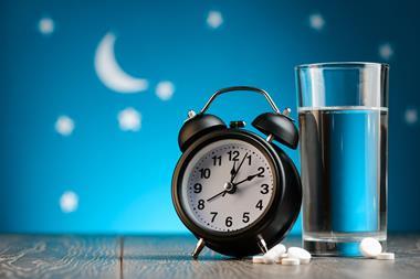 Alarm clock, pills and glass of water on a bedside table