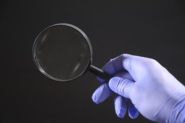 A hand in a latex glove holding a magnifying glass