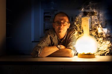 Moody and atmospheric portrait of Chemistry World columnist Andrea Sella, leaning on a worktop, illuminated by a flask.