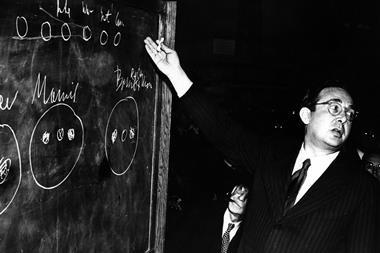Leo Szilard stands on the right, gestering towards a chalkboard with a piece of chalk in his hand