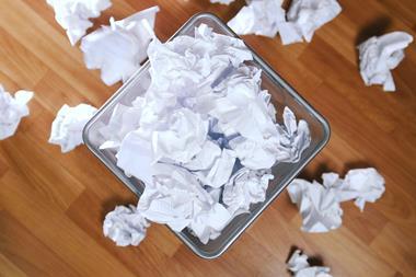 A waste paper basket overflowing with balled up paper