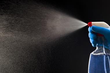 A photograph of a gloved hand spraying a chemical from a plastic bottle