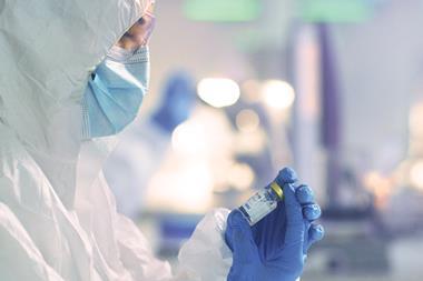 A scientist wearing PPE inspecting a glass vial