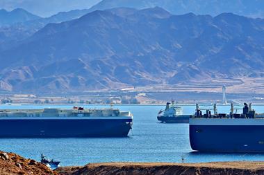 Large ships sailing past an arid, mountainous landscape