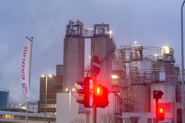 Red traffic light in front of Evonik flag and factory