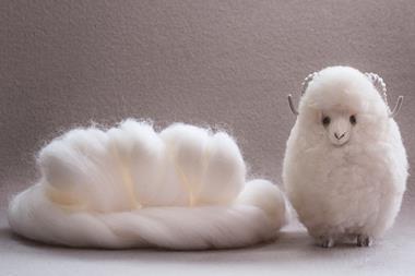 Roll of white wool next to a handmade woollen sheep, set on a neutral background