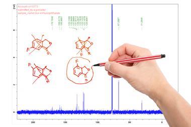 A printout of a carbon NMR spectrum. There are several different hand-drawn structures on one side, most of them crossed out. A hand holding a red pen is circling one of the structures