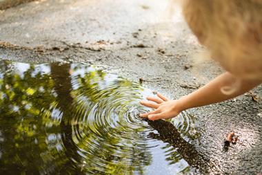 Child's hand touching water from a puddle