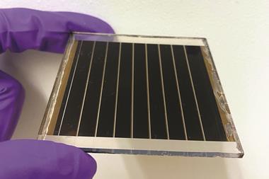 Close up of a hand in a purple latex glove holding a small solar cell