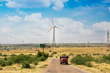 Red truck on rural Indian road with wind turbines in grassy landscape