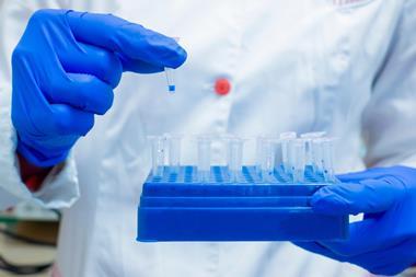 Chemist holding a tray of vials in one hand, removing one vial from the tray with the other hand
