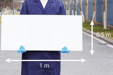 A man in a blue lab coat and latex gloves holding a white board 1 m by 0.5 m