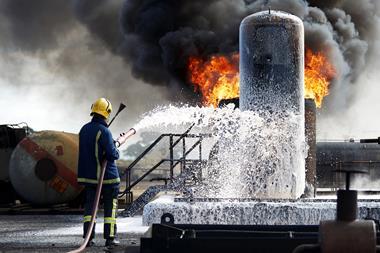 A firefighter sprays foam from a hose over a blaze on some chemical containers