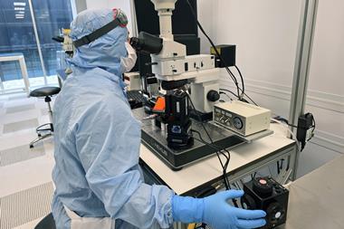 A scientist in full PPE looks through the scope on a microscope