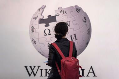 An image showing a woman standing in front of Wikipedia sign