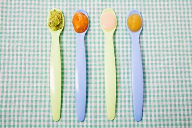 A photo of four plastic baby spoons each with a different food on the end