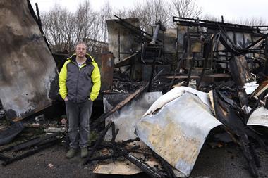 A man stands in front of a building that's burned down