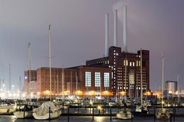 An old fashioned gas power station with boats in a harbour in front