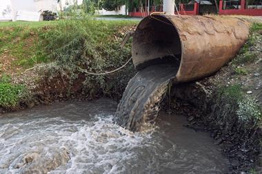 A sewage pipe empyting into a river near some buildings