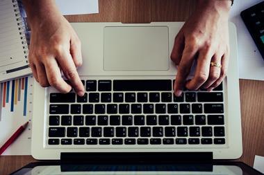 An image showing a man's hands typing on a laptop keyboard