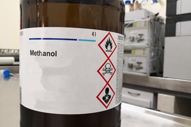 A bottle of methanol with hazard symbols warning it is flammable, toxic and health hazard on its label in a lab.