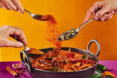 An image showing hands placing spices into a pan of curry