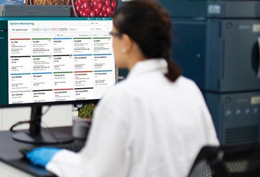 Scientist in lab monitoring multiple instruments using Waters System Monitoring software on a desktop screen