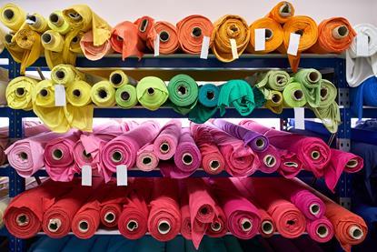 Blue shelves with bright multicolored fabric rolls on the light wall background inside a warehouse