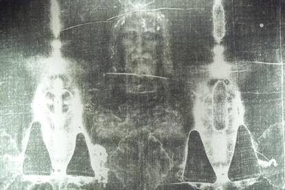 An enhanced black and white image of the Turin Shroud featuring a faint image of a bearded man's face some a damaged cloth