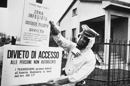 A black and white image of a policeman in Seveso, Italy pinning up warning signs written in Italian warning of chemical contamination of the area