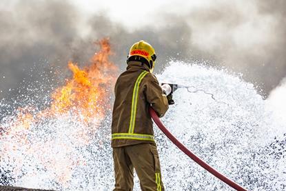 A firefighter uses foam from a powerful hose to tackle an outdoor blaze