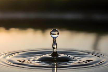 A single water droplet creates ripples on a serene lake surface at sunset