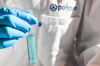 A close up of a person wearing a branded Polypure lab coat holding a test tube of pale blue liquid