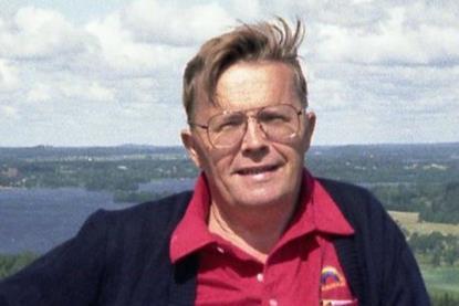 A headshot of Martti Harmoinen wearing a red shirt and black cardigan in the countryside