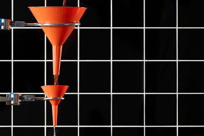 A picture showing the pour of liquid through funnels into glass flask