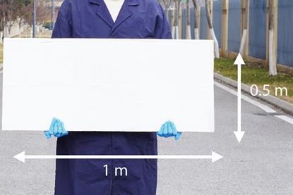A man in a blue lab coat and latex gloves holding a white board 1 m by 0.5 m