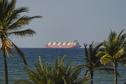 A tanker ship on the Strait of Hormuz in the ocean as seen from the shore where there are palm trees