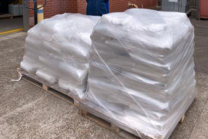 A man outside an industrial facility standing next to two pallets loaded with full sacks