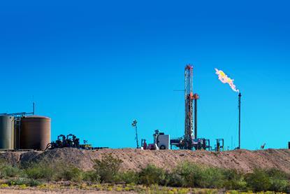 An oil drilling platform with a burning flare in a dry landscape under a clear blue sky
