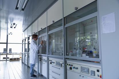 An image showing a male scientist writing with a sharpie on a fumehood sash inside a clean laboratory