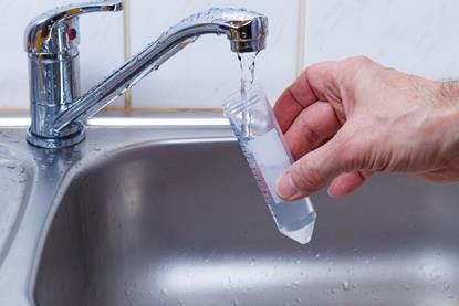 A hand filling a sample tube with water from a domestic tap