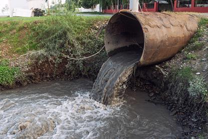 A sewage pipe empyting into a river near some buildings